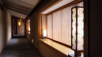 A corridor with a wooden floor, a wall with a window, and a traditional Japanese lantern.