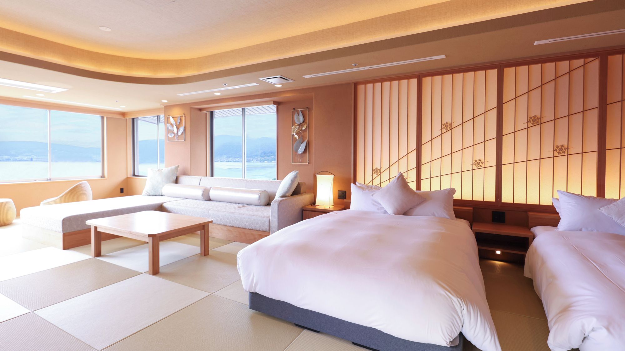 A modern hotel room with a large bed, a sofa, a coffee table, and a view of the sea.