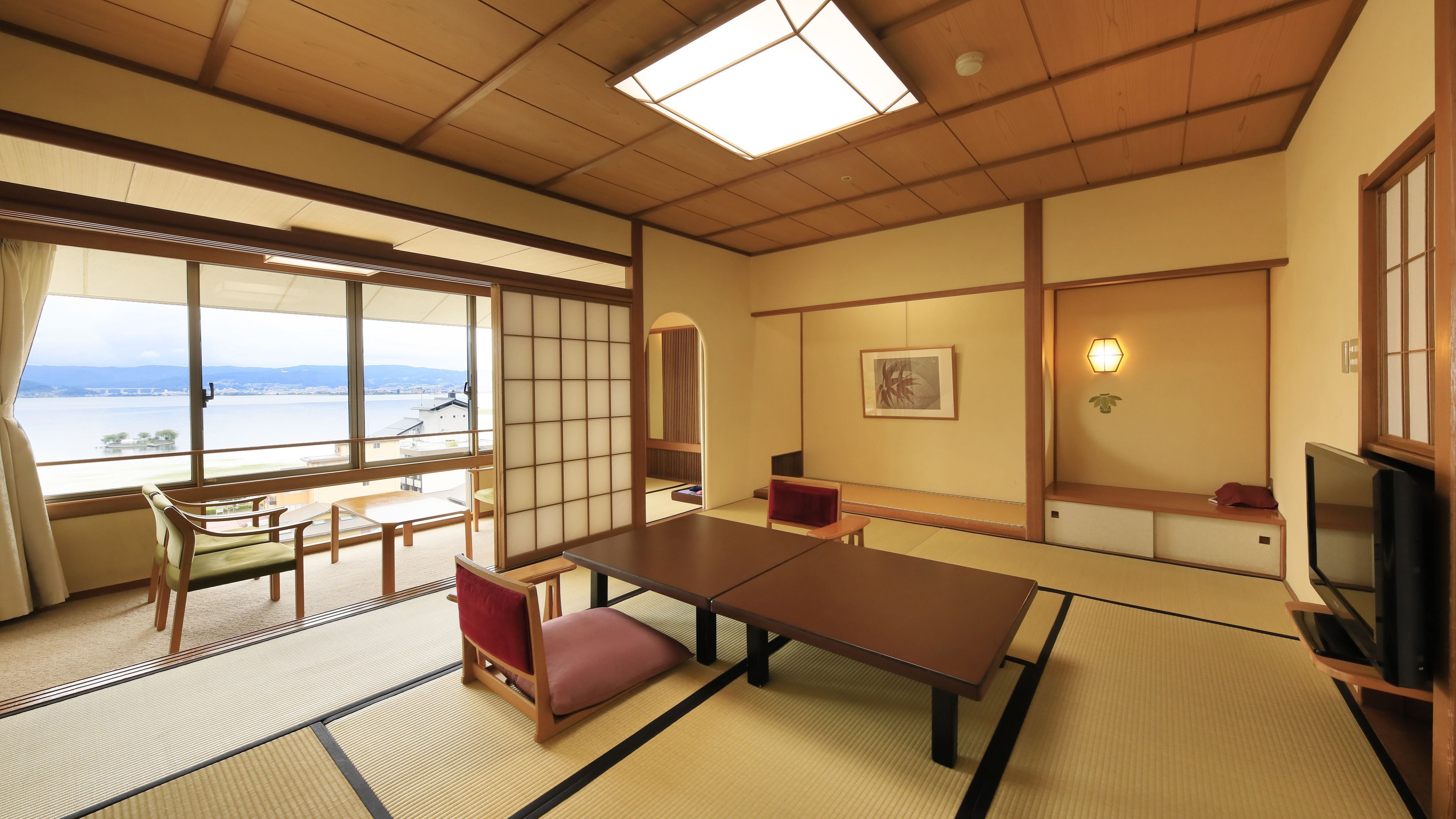 A traditional Japanese room with tatami flooring, a low table, a sofa, a television, and a view of a body of water.