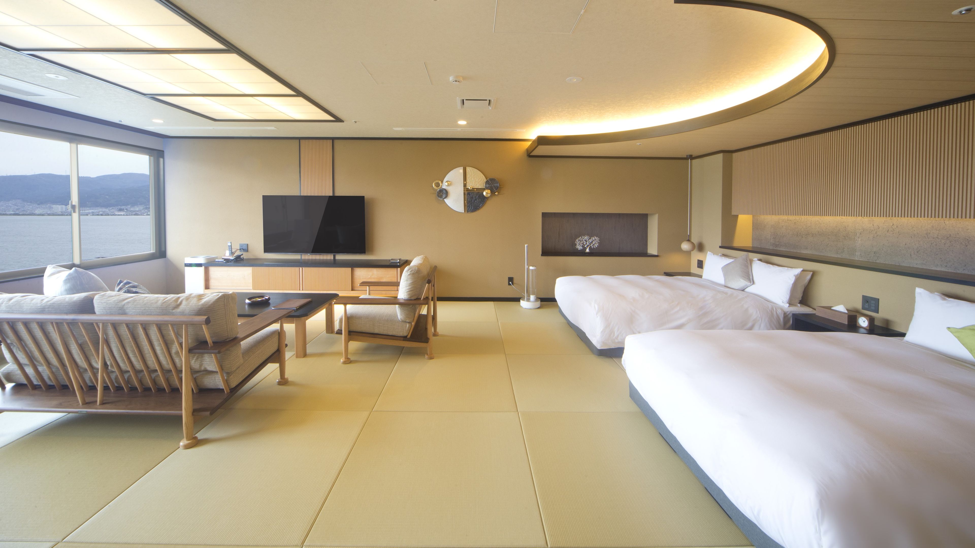 A hotel room with a bed, a desk, a chair, a television, and a view of the sea.