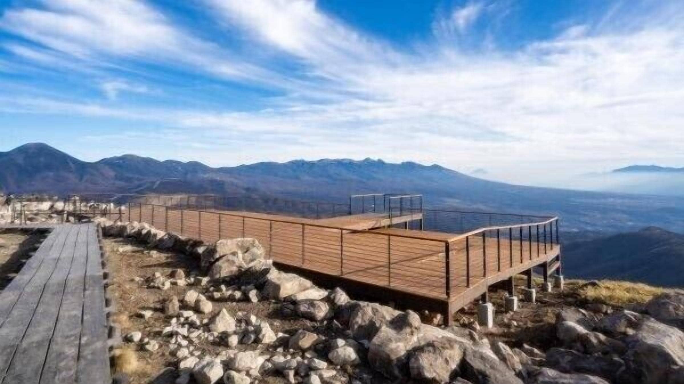 A wooden viewing platform with a metal railing, overlooking a mountainous landscape.