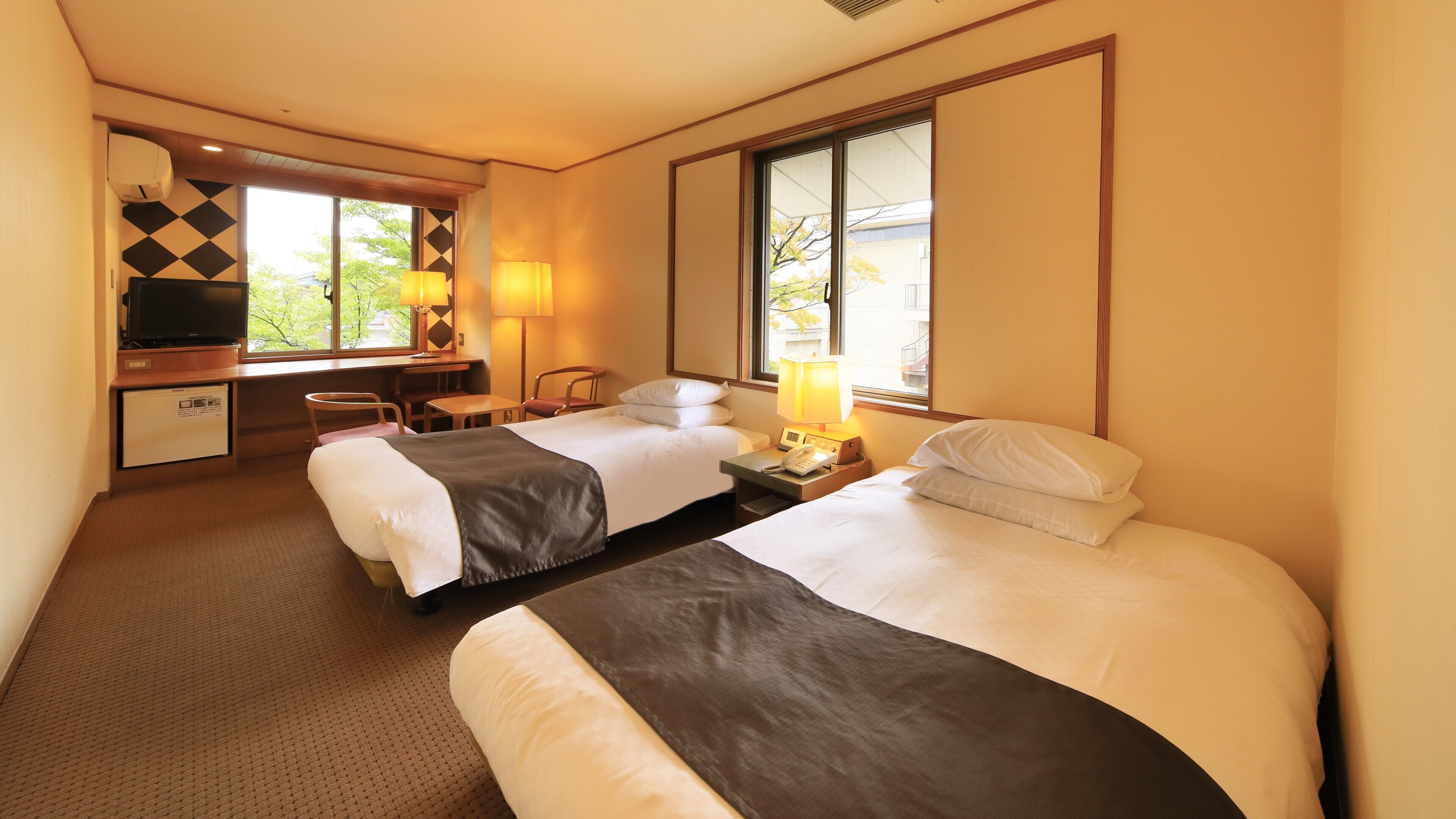 Habitación de hotel con dos camas, un escritorio con ordenador, una silla y una ventana con vistas.