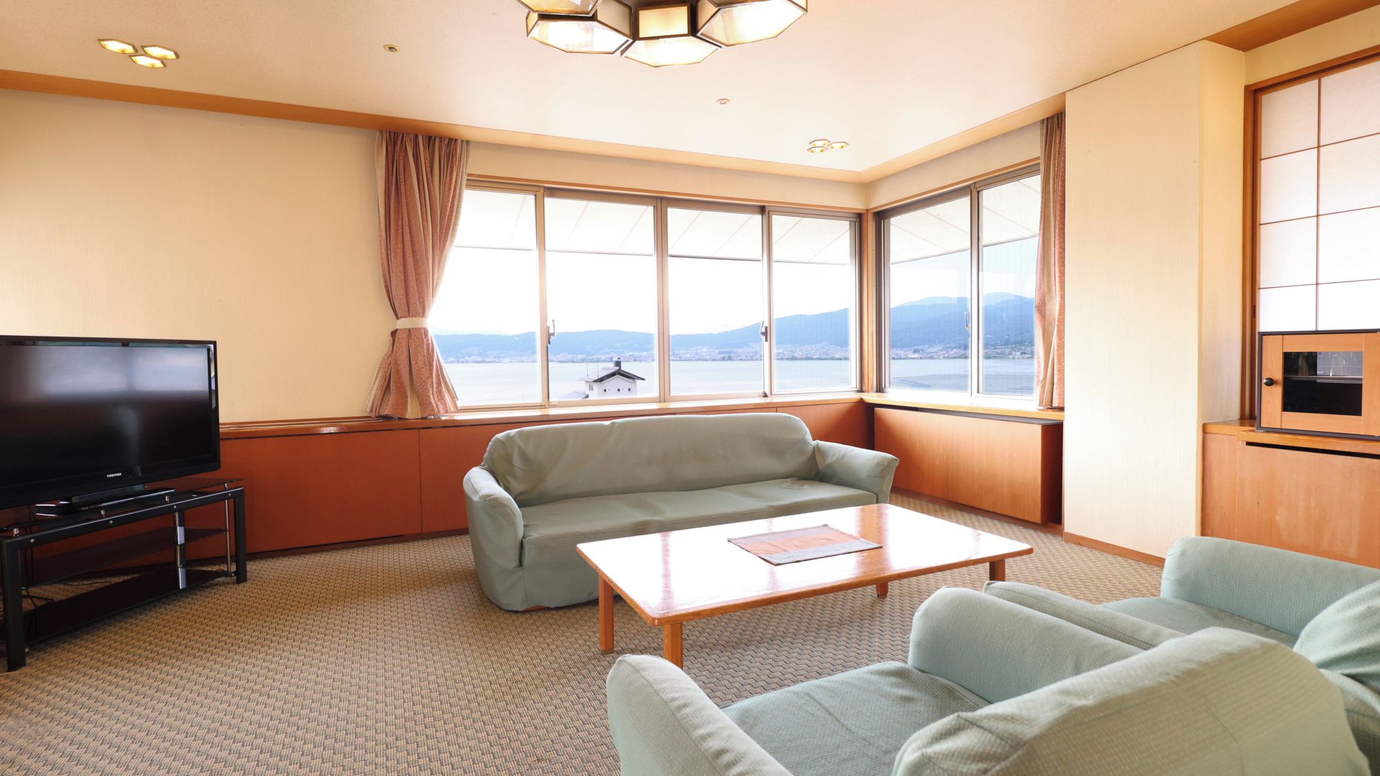 A hotel room with a large window, a flat-screen TV, a sofa, a coffee table, and a cabinet.