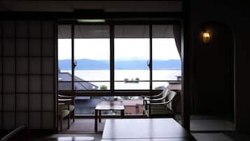 A room with a large window overlooking a body of water and mountains. There are two chairs and a table in the room.