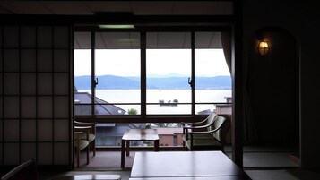 Una habitación con un gran ventanal con vistas a un cuerpo de agua y montañas. Hay dos sillas y una mesa en la habitación.