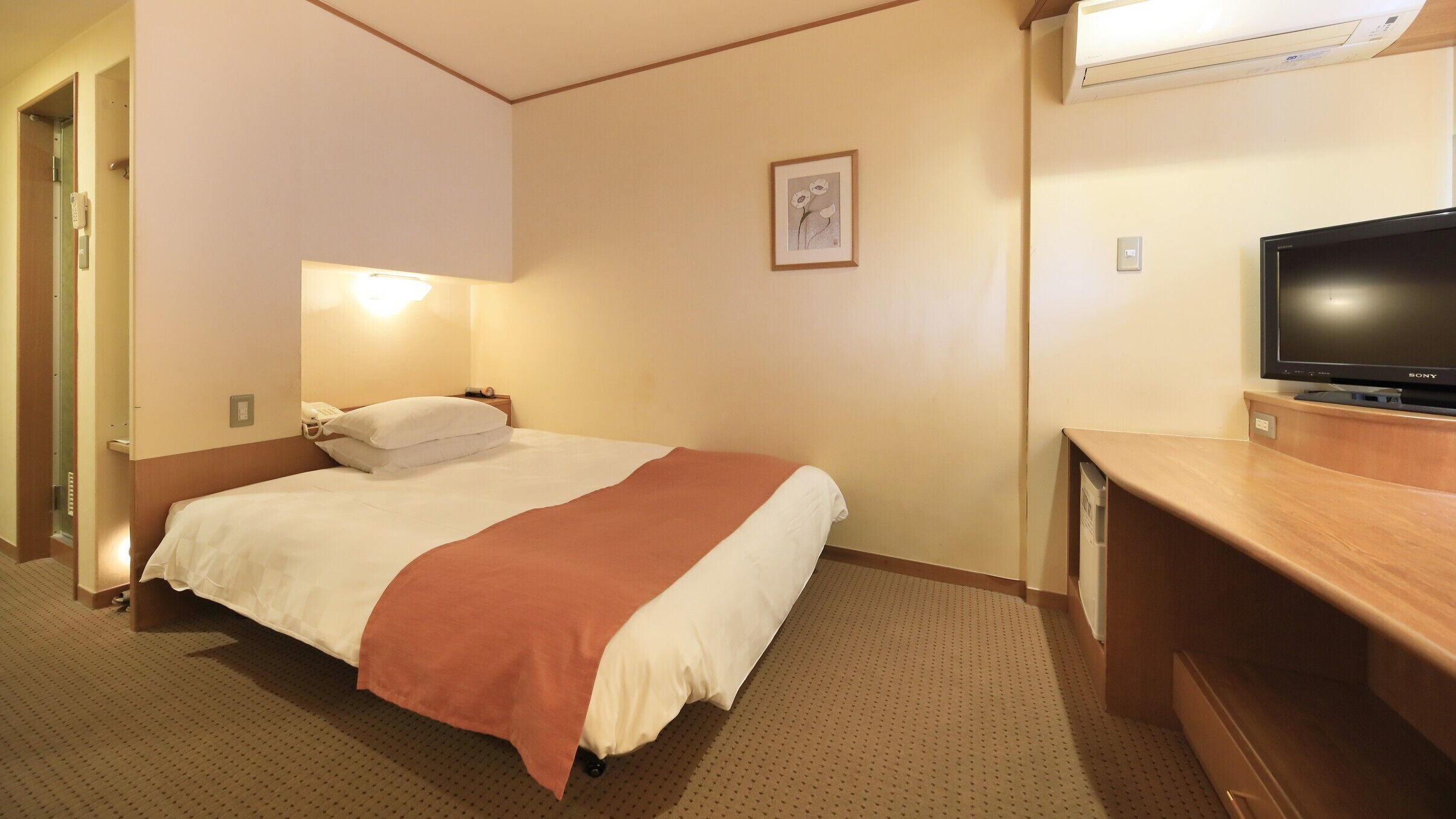 Habitación de hotel con cama, lámpara de noche, televisión y un cuadro en la pared.