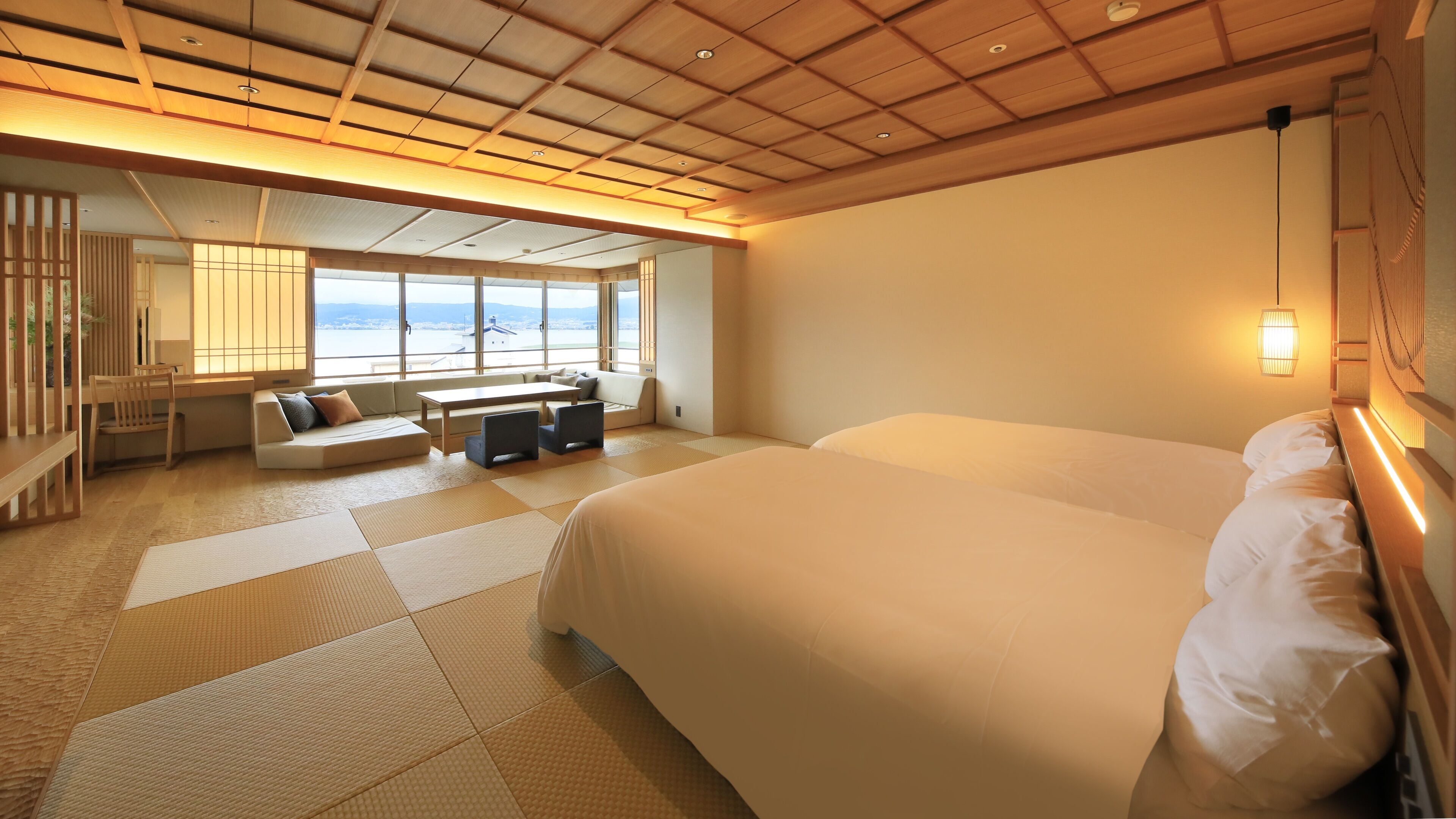 A hotel room with a large bed, a sofa, a dining table, and a view of the sea.