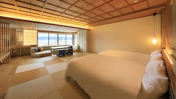 A hotel room with a large bed, a sofa, a dining table, and a view of the sea.