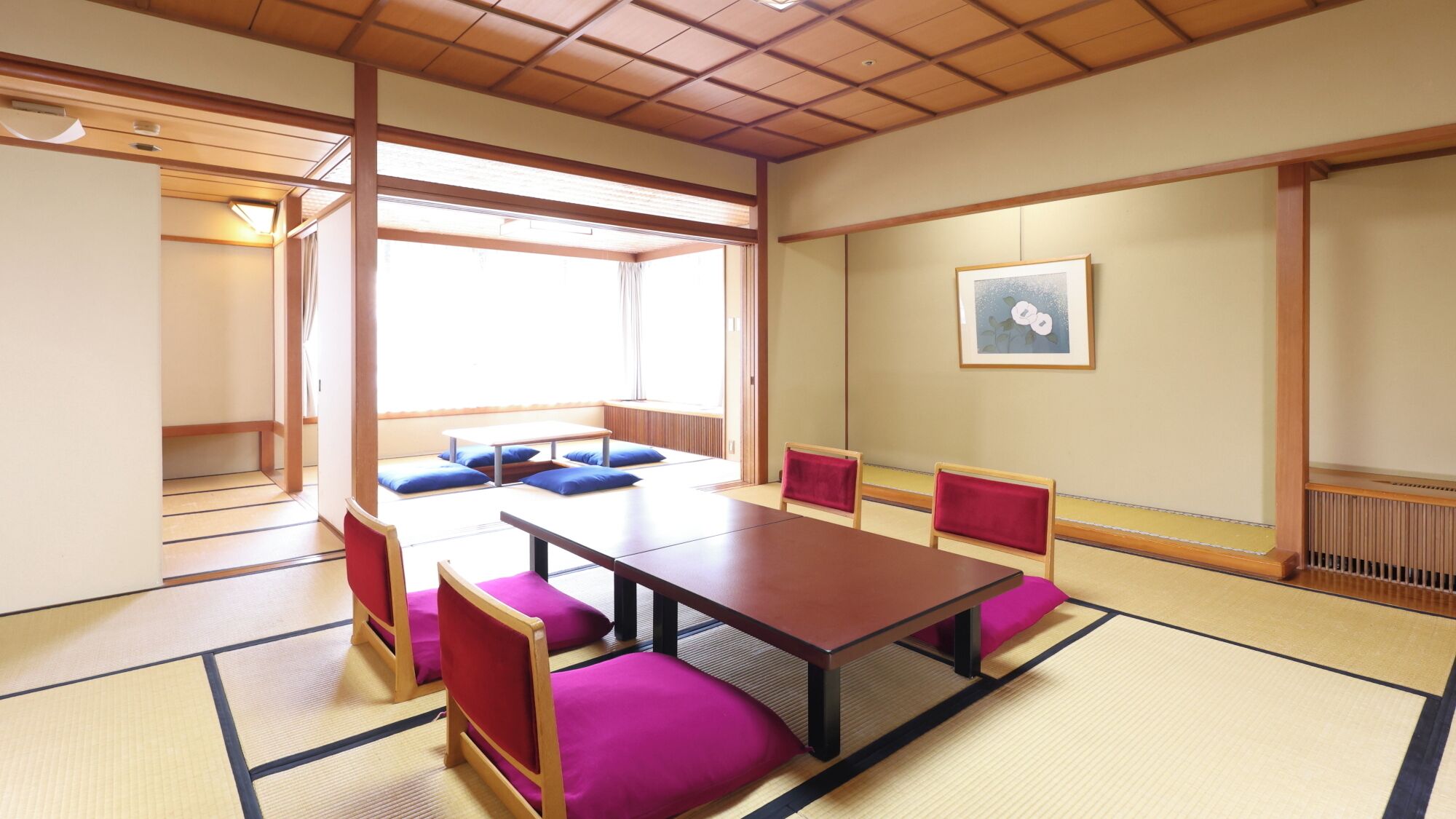 Una habitación con esteras de tatami, una mesa baja y sillas, un ventanal grande y un cuadro en la pared.