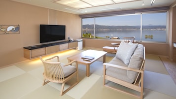 Una sala de estar moderna con un televisor de pantalla plana grande, un sofá, una mesa de centro y vistas a un lago y montañas.