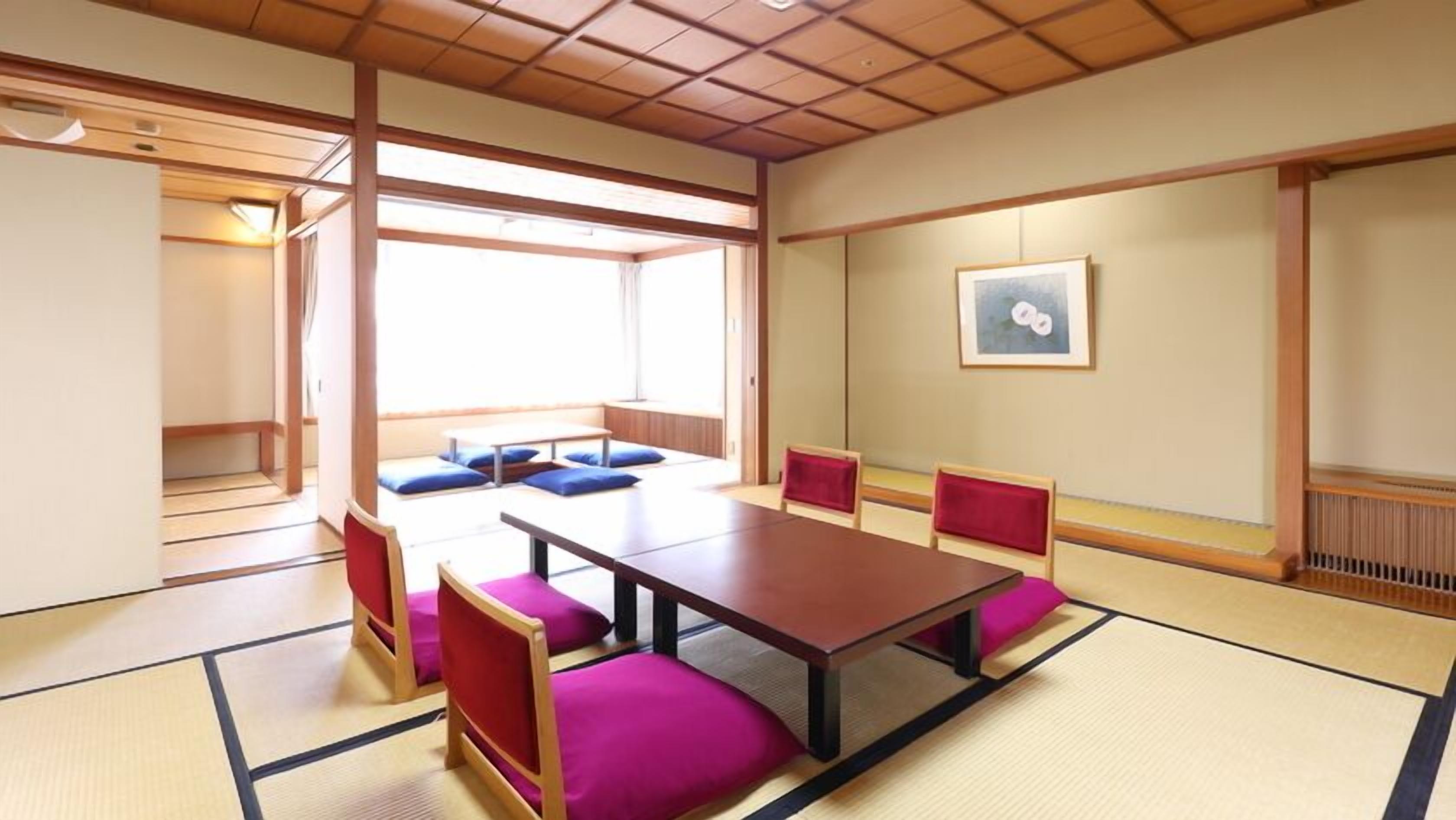 Una habitación japonesa tradicional con suelo de tatami, una mesa baja y cojines rojos.