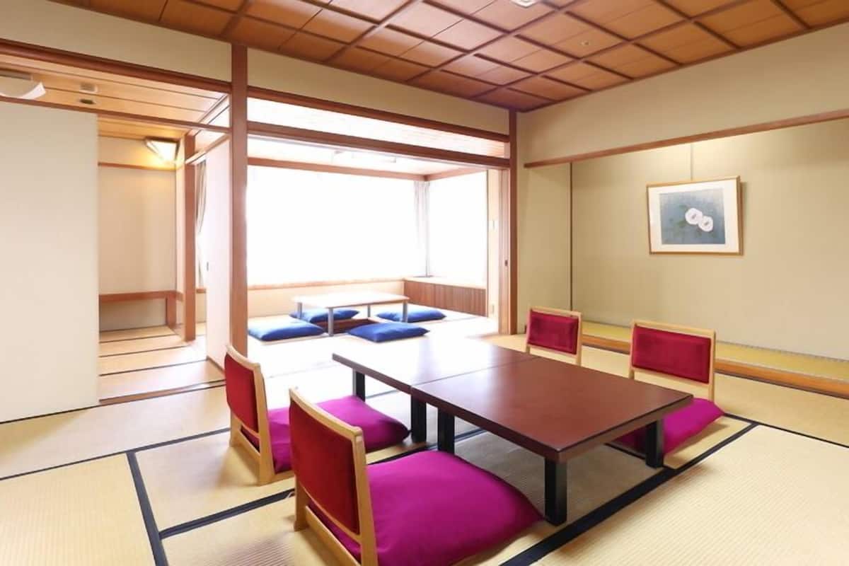 A traditional Japanese room with tatami flooring, a low table, and red cushions.