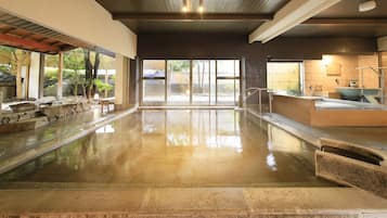 Un espace piscine intérieure propre, avec des parois en verre transparent, une piscine bordée de pierres et un sauna situé à droite.