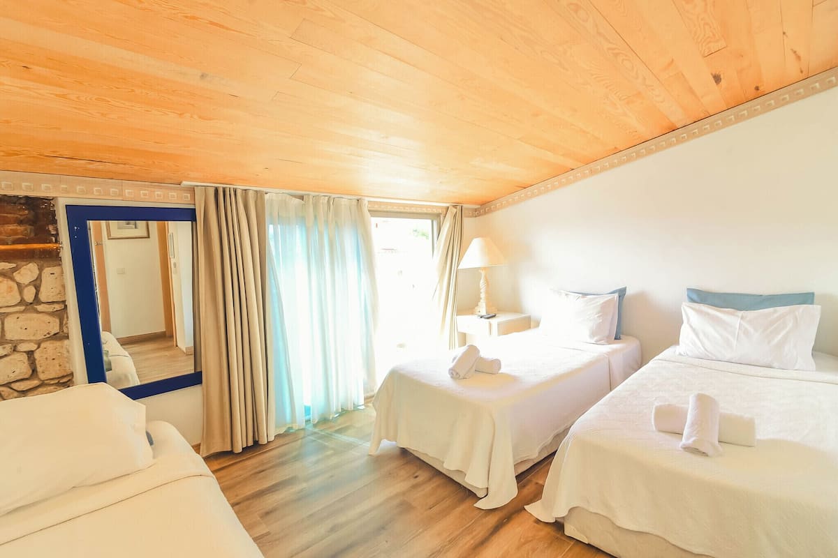 A hotel room with two beds, a stone wall, a wooden ceiling, and a large mirror.