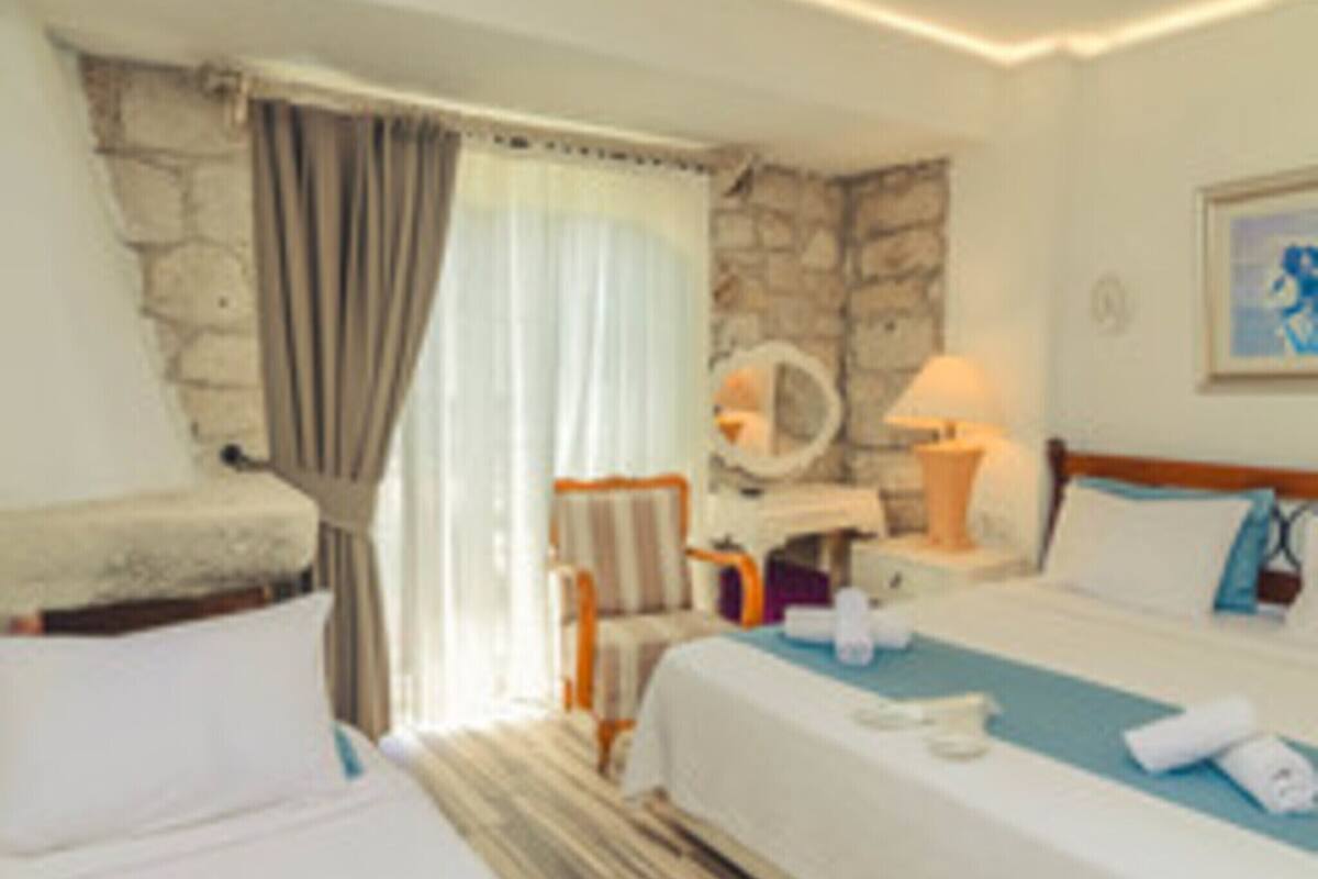 A hotel room with a bed, a chair, a table, and a stone wall.