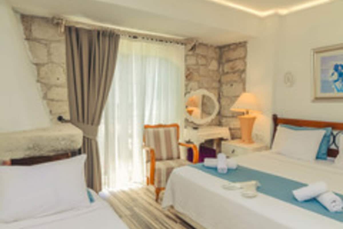 Una habitación de hotel con una cama, una silla, una mesa y una pared de piedra.