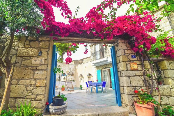 A stone archway with a blue door, a table and chairs outside, and potted plants.