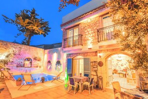 A two-story stone building with a swimming pool, outdoor seating, and a balcony.