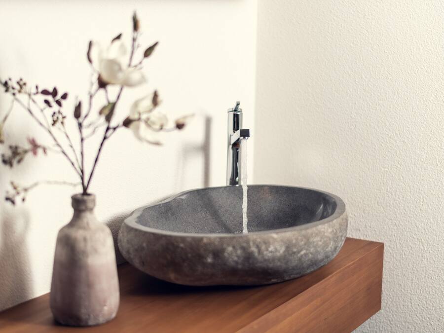 A stone sink with a faucet on a wooden shelf.