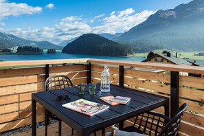 A wooden deck with a table and chairs, overlooking a lake and mountains. - Conrad's Mountain Lodge (Silvaplana)