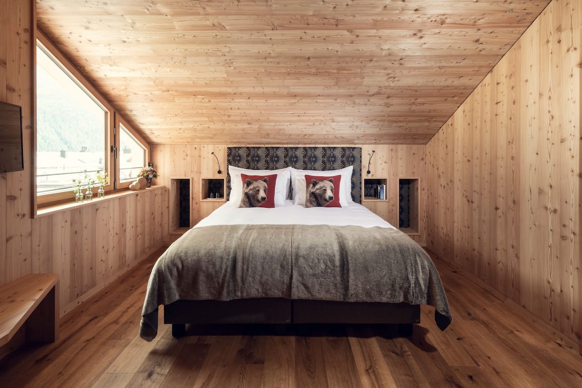 A wooden-paneled bedroom with a large bed, wooden nightstands, and a window with a view of the outdoors.