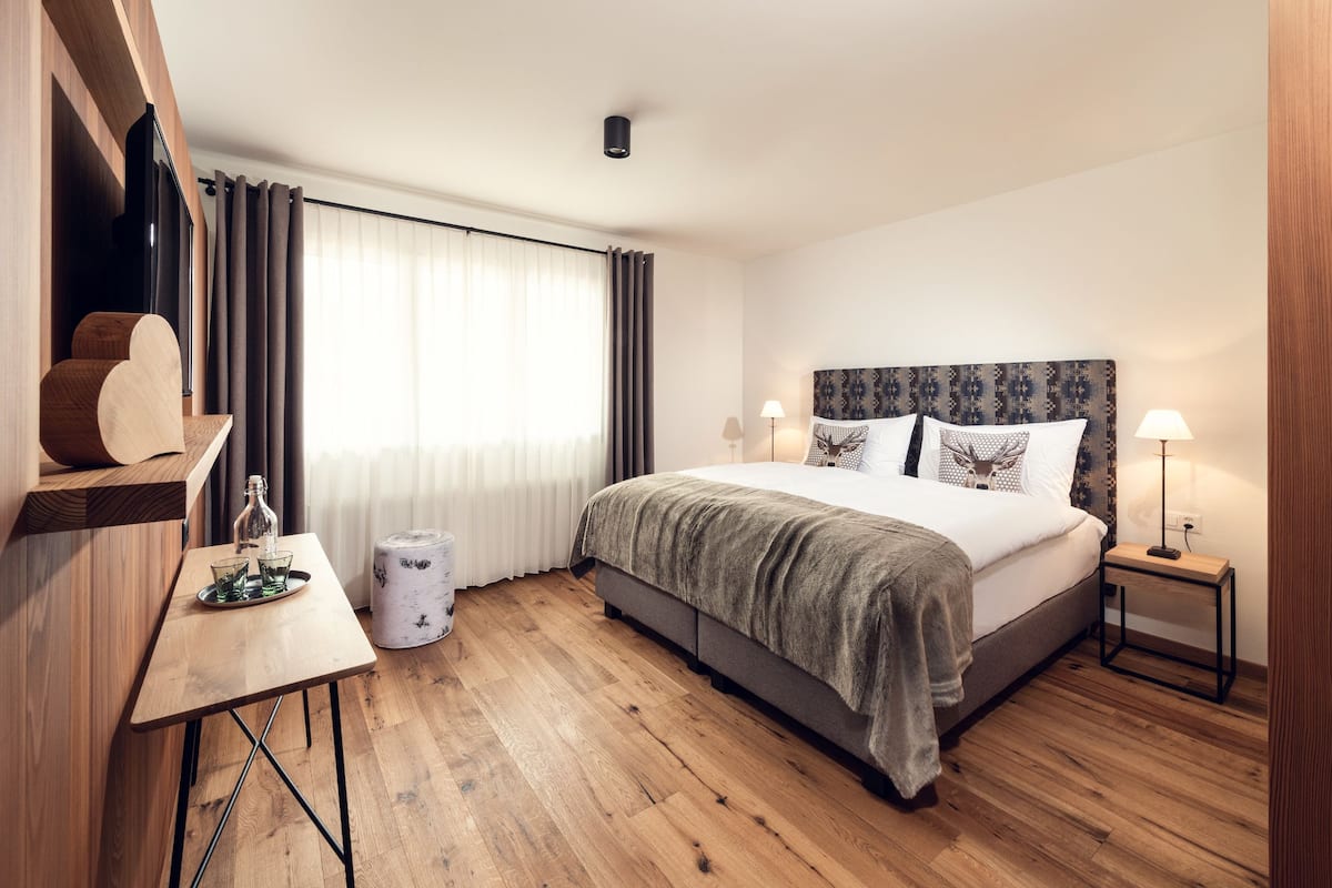 A modern hotel room with a large bed, a wooden desk, and a window with curtains.