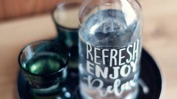 A clear glass bottle with a label that reads "REFRESH ENJOY Relax" on a black tray.