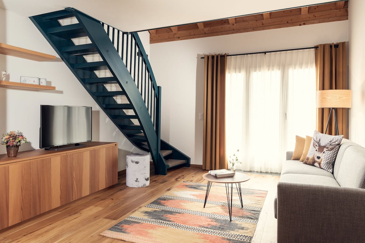A modern living room with a wooden floor, a staircase, a sofa, a TV, and a lamp.