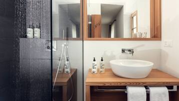 A modern bathroom with a glass-enclosed shower, a wooden vanity with a white sink, and two bottles of shampoo.