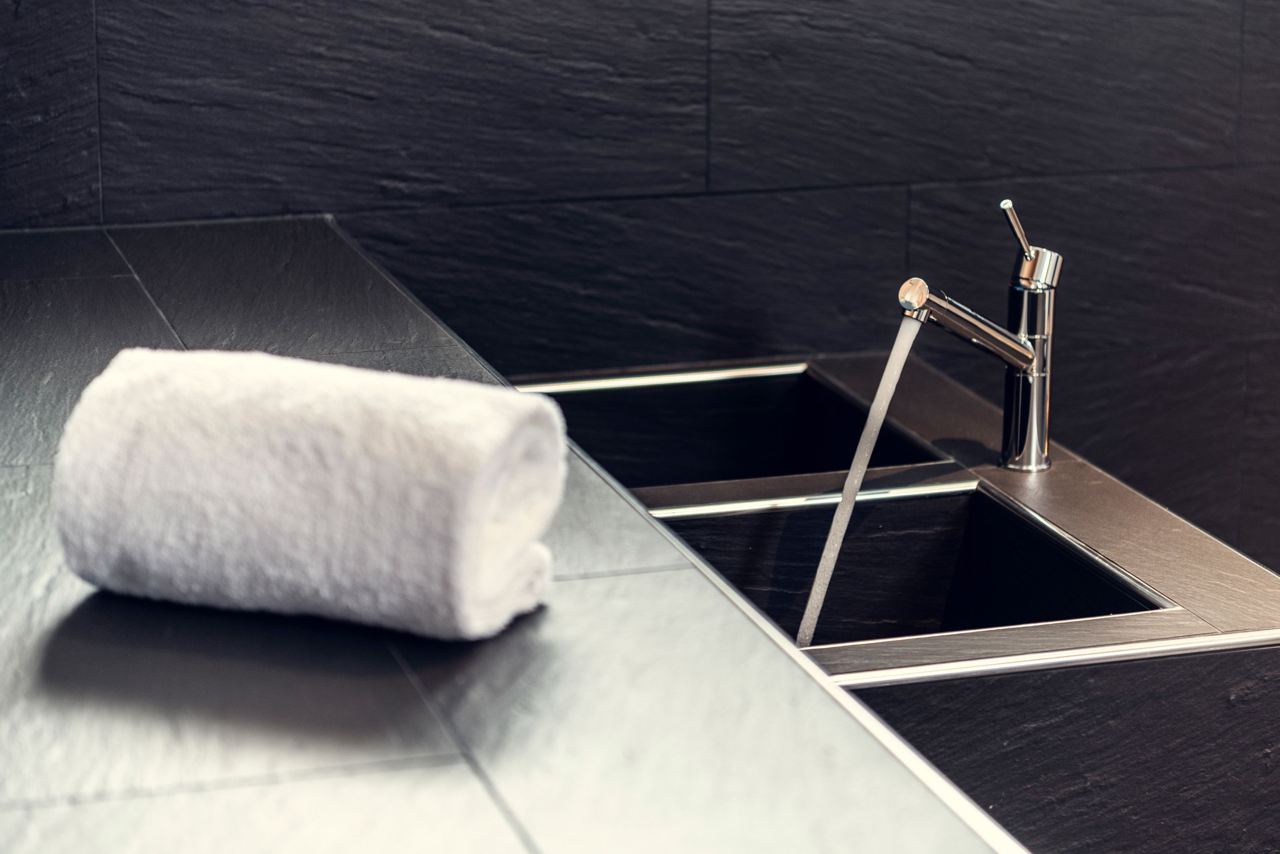 Une salle de bain moderne avec un sol carrelé de noir, un évier en acier inoxydable et une serviette blanche.