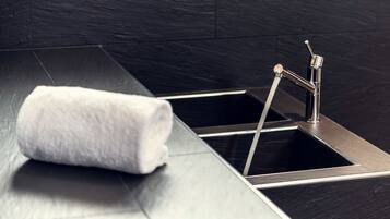 Une salle de bain moderne avec un sol carrelé de noir, un évier en acier inoxydable et une serviette blanche.