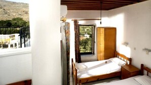 A bedroom with a wooden bed, a wardrobe, and a balcony with a view of the landscape. - Lindos Marianthi Studios (Rhodes)