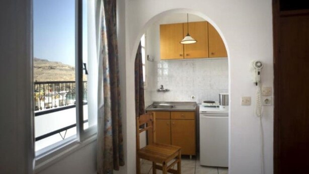 A compact kitchen with an arched doorway, a wooden chair, and a view through a window. - Lindos Marianthi Studios (Rhodes)