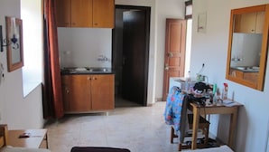 A compact kitchen with wooden cabinets, a sink, and a table with various items. - Lindos Marianthi Studios (Rhodes)