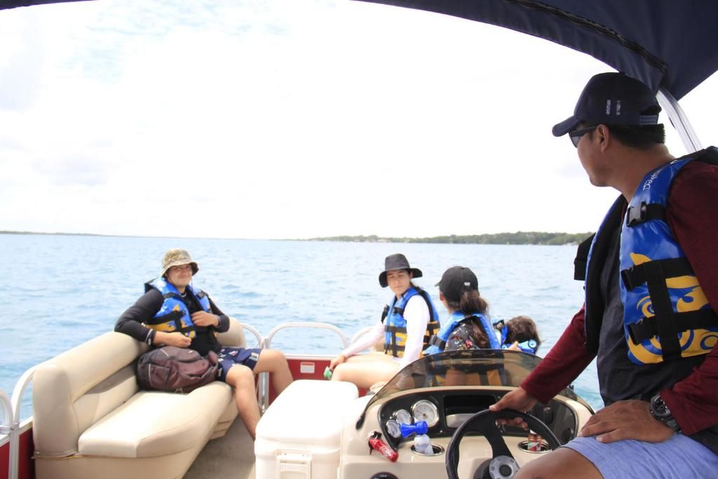 A boat with passengers wearing life jackets, a steering wheel, and a water container on the deck.