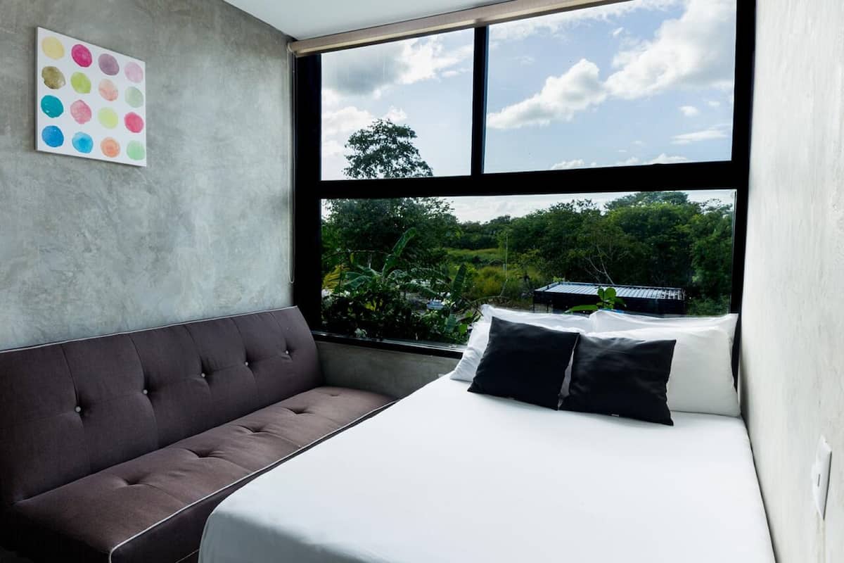 Ein modernes Schlafzimmer mit großem Fenster, einem grauen Sofa und einem Bett mit weißer und schwarzer Bettwäsche.