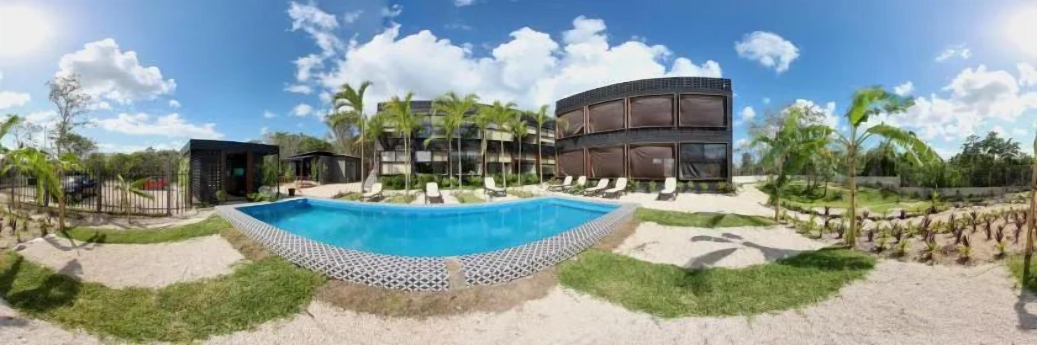 A swimming pool with lounge chairs, a building with multiple floors, and palm trees.
