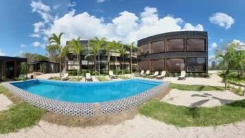 A swimming pool with lounge chairs, a building with multiple floors, and palm trees.