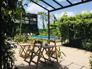 Un área de estar al aire libre con piscina, rodeada de vegetación y un edificio moderno.