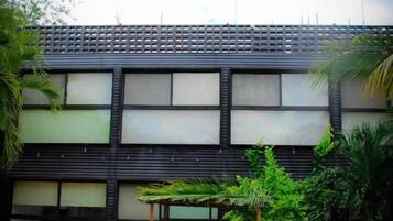 Una piscina con una persona recostada en el borde, rodeada de follaje y un edificio con amplios ventanales.