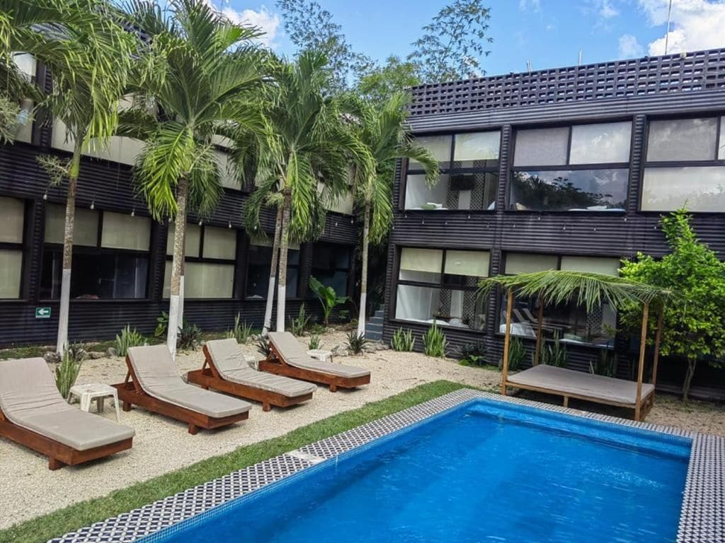 Un bâtiment moderne doté d’un espace piscine, comprenant des chaises longues et des palmiers.
