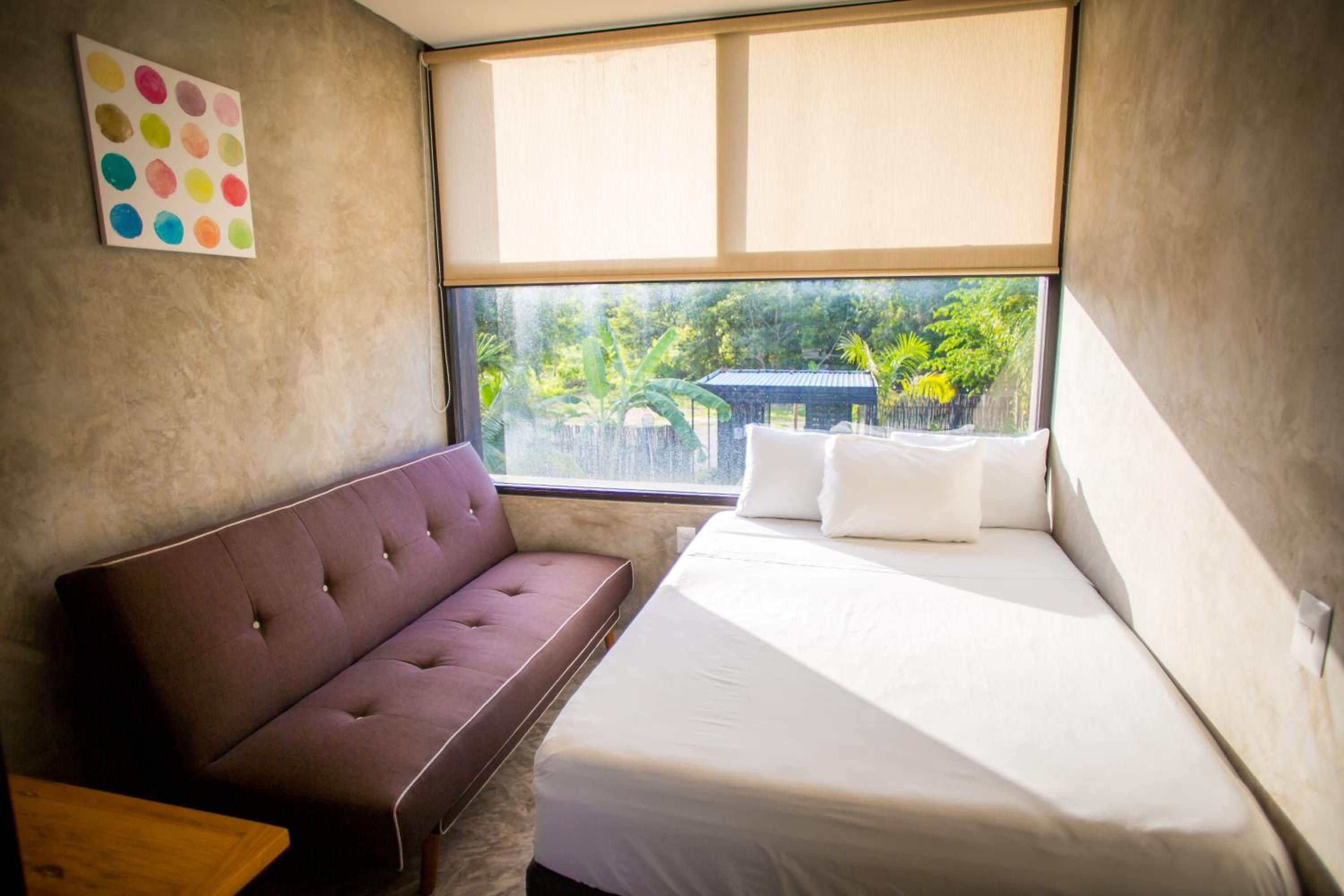 Una habitación con cama, un banco acolchado y una ventana que da a zonas verdes.