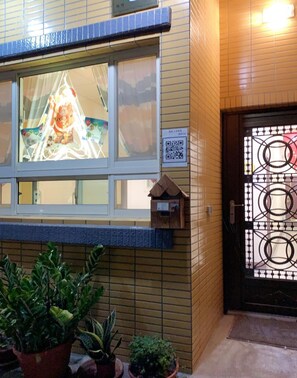 A building facade with a window displaying a colorful interior scene, a small mailbox, and potted plants at the entrance. - Luyu Homestay (Lukang)