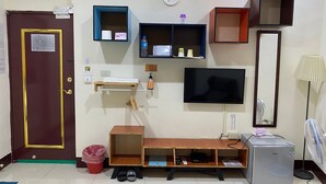 A hotel room with a wooden door, a TV, a small fridge, a desk with a chair, and a shelf with toiletries. - Luyu Homestay (Lukang)