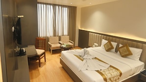 A hotel room with a bed, a desk, a chair, a television, and a window with curtains. - Hotel Simran Heritage (Raipur)