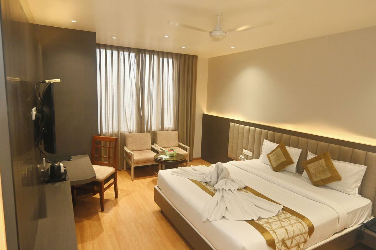 A hotel room with a bed, a desk, a chair, a television, and a window with curtains.
