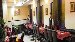 A restaurant with tables set for dining, a waiter in uniform, and a waiter standing by the wall. - Hotel Simran Heritage (Raipur)