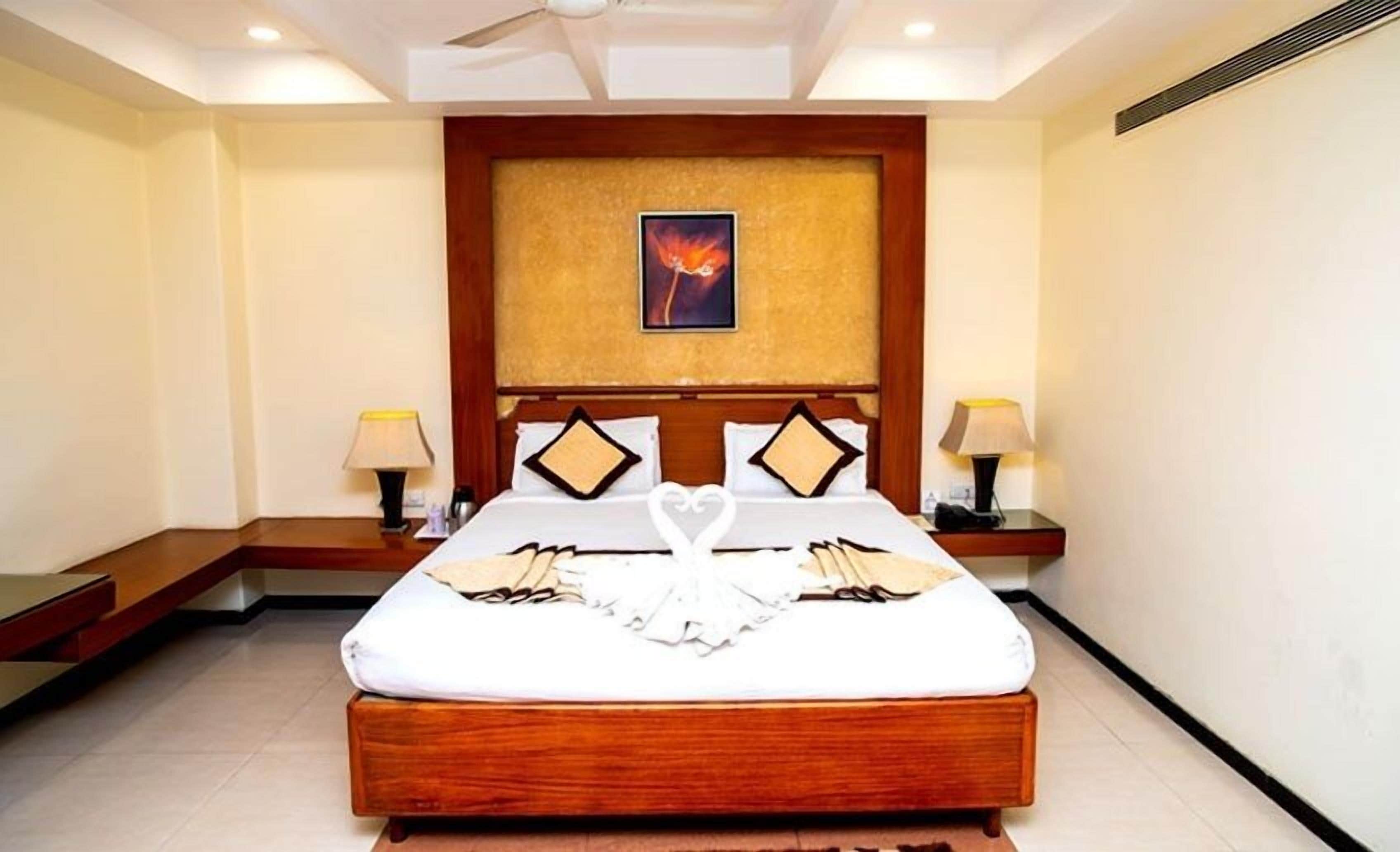 Quarto de hotel com uma cama grande, duas mesas de cabeceira, um ventilador de teto e uma obra de arte emoldurada acima da cama.
