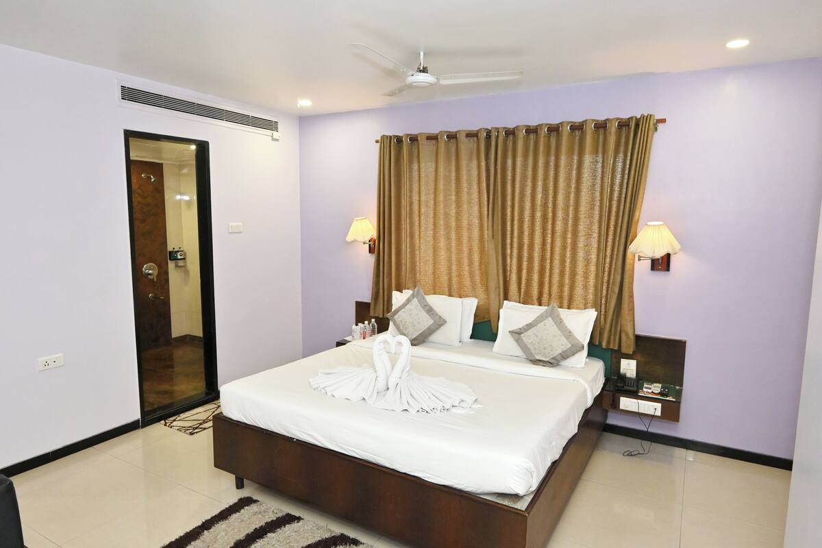 A hotel room with a bed, two bedside lamps, a ceiling fan, and a door leading to another room.