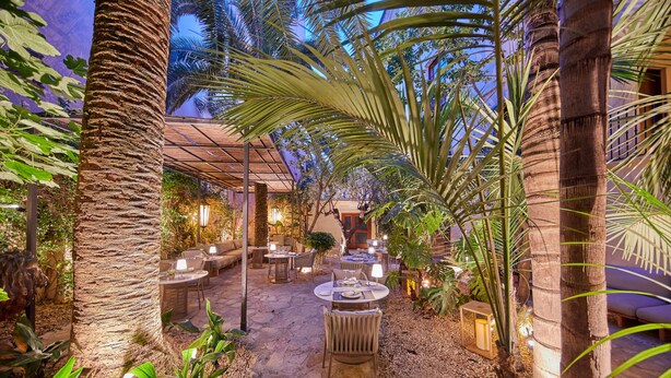 An outdoor patio area with stone flooring, round tables, wicker chairs, and ambient lighting. - Palacio Can Marqués (Palma de Mallorca)